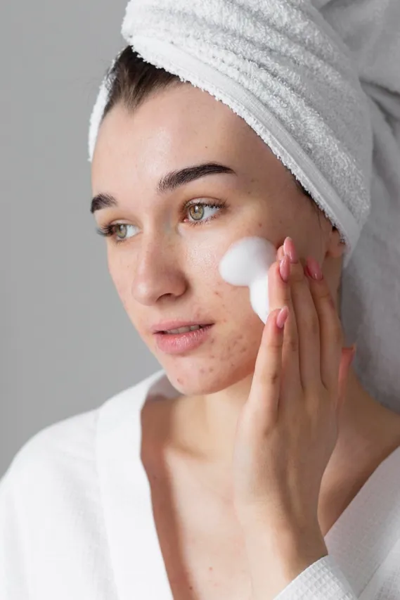 Young woman in a bathrobe with a towel in her hair, massaging a foaming facial cleanser onto her face – gentle cleansing for acne-prone skin