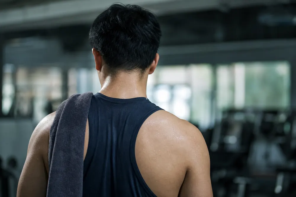 The back of a young adult seen from behind after training, with sweaty skin, in a tight sports top and with a towel over the shoulder