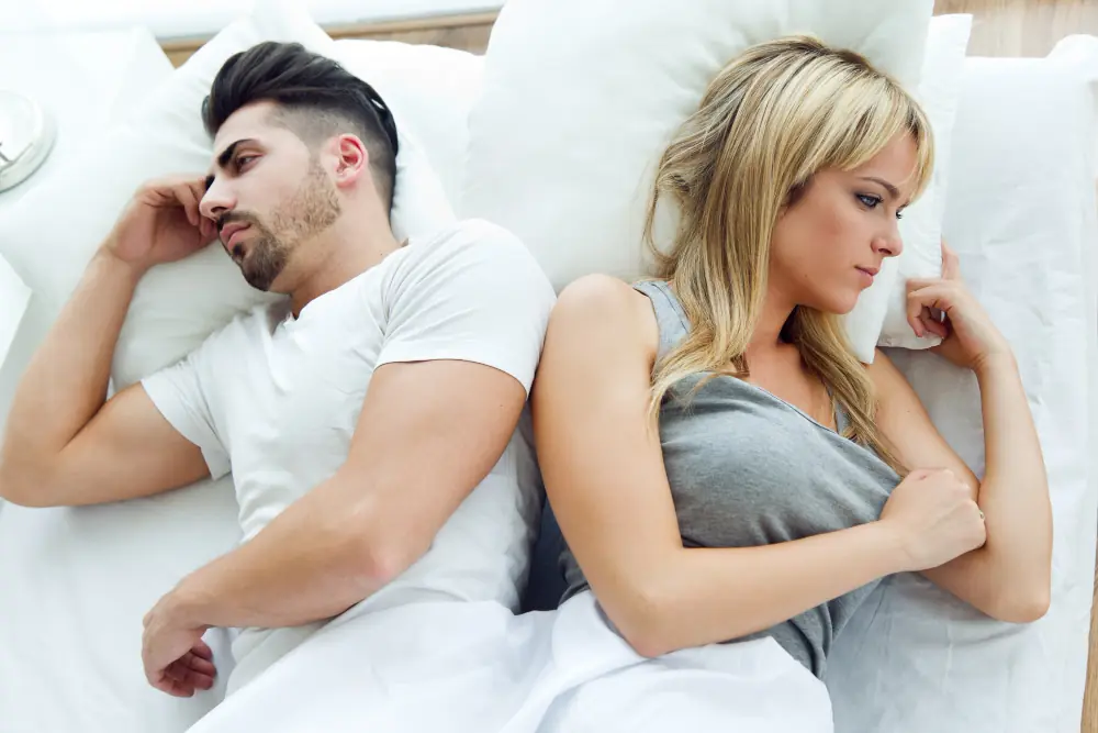 A young couple lying back to back in bed, both looking ahead