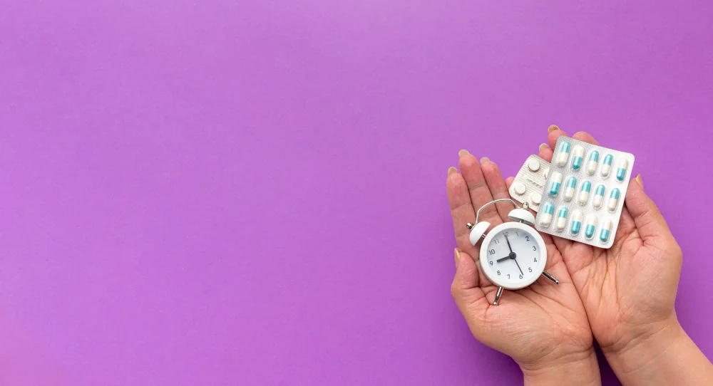 Hands holding a small white alarm clock and two blister packs of pills against a purple background – with emergency contraception, time is the decisive factor